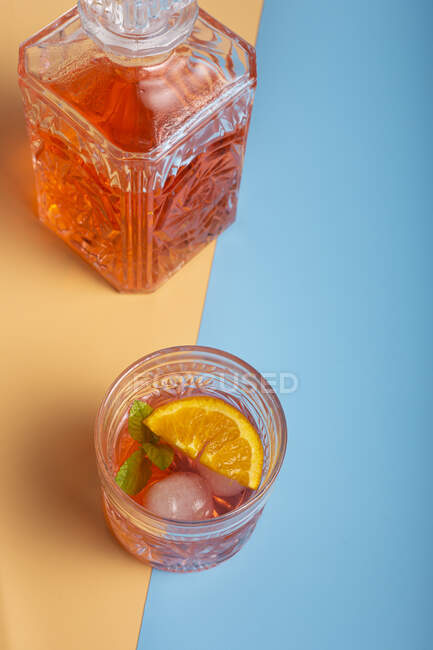 Cóctel de naranja fría fresca en jarra y taza de vidrio con cubitos de hielo - foto de stock
