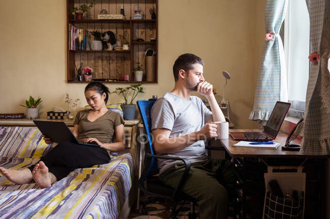 Занимательная пара предпринимателей в повседневной одежде, сидящих в спальне и работающих в Интернете, просматривая компьютер — стоковое фото