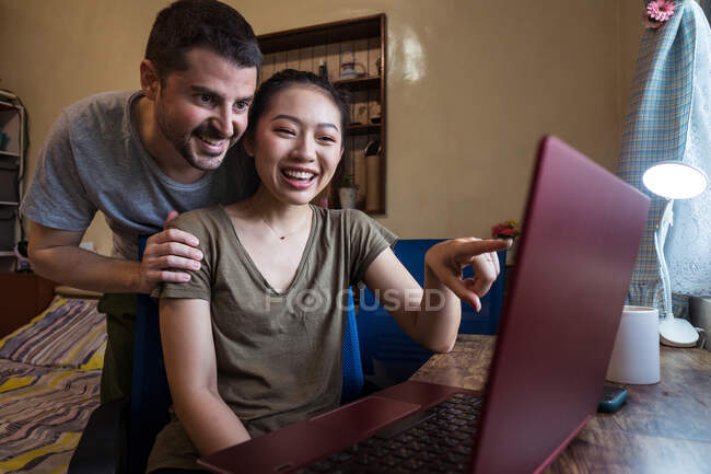 Low angle of happy boyfriend helping asian girlfriend working on the computer at home — Stock Photo