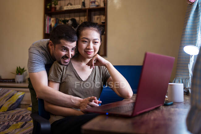 Низкий угол счастливого парня, помогающего азиатской девушке работать за компьютером дома — стоковое фото
