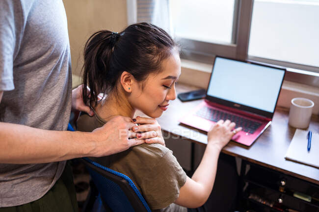 Сверху женщина-предприниматель в повседневной футболке сидит за столом с компьютером и работает на стартапе при прикосновении руки бойфренда — стоковое фото
