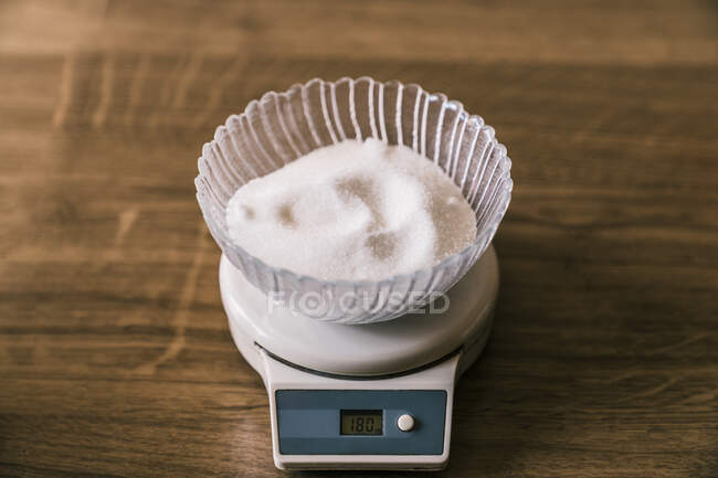 From above of glass bowl with white sugar placed on electronic kitchen scales showing 180 on wooden table — Stock Photo