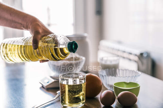 Ernte anonyme Frau gießt Pflanzenöl in Maßglas auf den Tisch mit Zutaten für Rezept während der Zubereitung von Gebäck zu Hause — Stockfoto