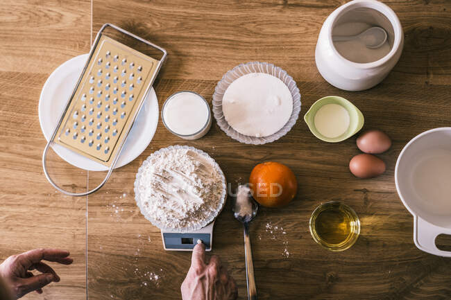 Vista dall'alto del raccolto anonimo femminile che pesa farina di frumento su bilance elettroniche mentre prepara ingredienti per deliziosi muffin aromatici fatti in casa in cucina — Foto stock