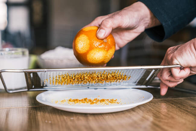Vue latérale de la culture femme anonyme enlever zeste d'orange avec râpe tout en préparant la pâtisserie aromatique dans la cuisine à la maison — Photo de stock