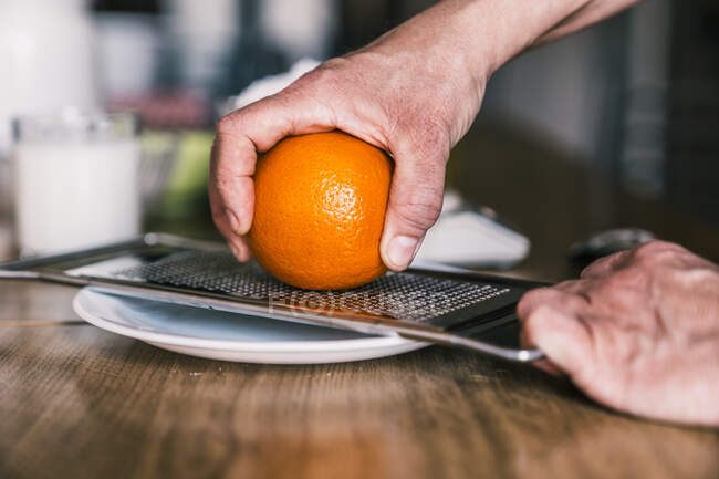 Vista laterale della donna anonima raccolto rimozione scorza d'arancia con grattugia durante la preparazione di pasticceria aromatica in cucina di casa — Foto stock