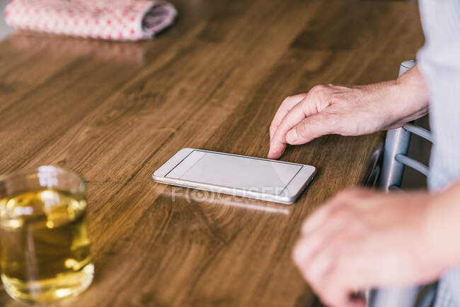 Anonyme reife Frau in Schürze mit Smartphone ernten und Rezept lesen, während sie am Küchentisch mit Zutaten zum Backen steht — Stockfoto