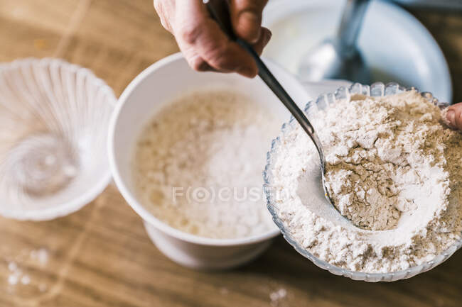 De cima confeiteiro irreconhecível em avental de pé na cozinha com tigela de vidro e adicionando farinha com colher enquanto prepara a massa para muffins — Fotografia de Stock