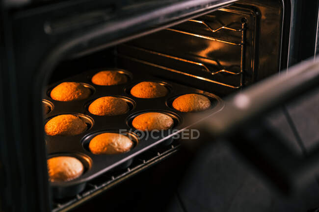 Cosecha irreconocible confitero sacar del horno deliciosos panecillos caseros en la cocina - foto de stock