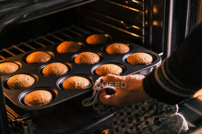 Cultivar confeiteiro irreconhecível tirando do forno deliciosos muffins caseiros na cozinha — Fotografia de Stock