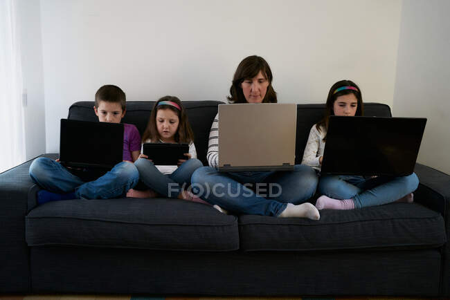 Серйозна мати і діти проводять час разом, використовуючи гаджети на дивані вдома — стокове фото