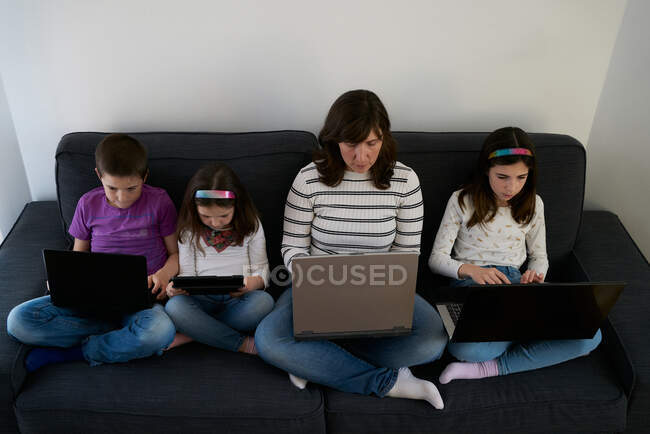 Serious mother and kids spending time together using gadgets on sofa at home — Stock Photo