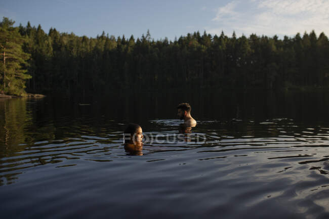 Vista lateral do homem e da mulher nadando juntos na água limpa calma do lago da floresta no dia ensolarado no verão durante as férias — Fotografia de Stock