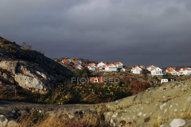 Paisaje rocoso con casas de pueblo a la luz del sol y cielo nublado oscuro - foto de stock