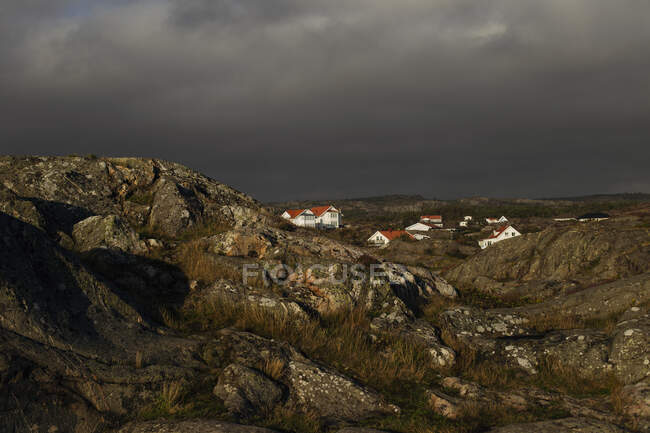 Paisaje rocoso con casas de pueblo a la luz del sol y cielo nublado oscuro - foto de stock