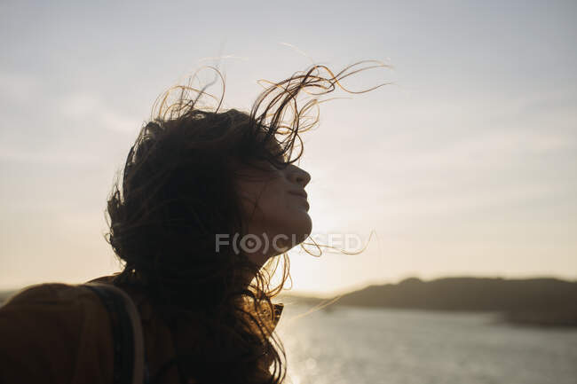 Вид сбоку женщины в повседневной одежде, стоящей на набережной и наслаждающейся бризом в солнечный день и отводящей взгляд — стоковое фото