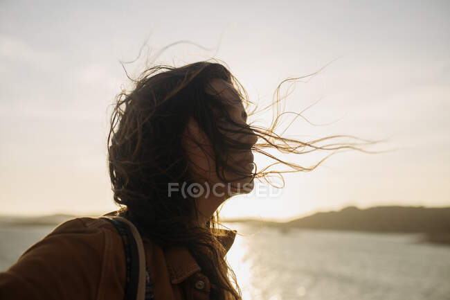 Vista laterale della femmina che indossa abiti casual in piedi sulla banchina e gode della brezza nella giornata di sole e distogliendo lo sguardo — Foto stock
