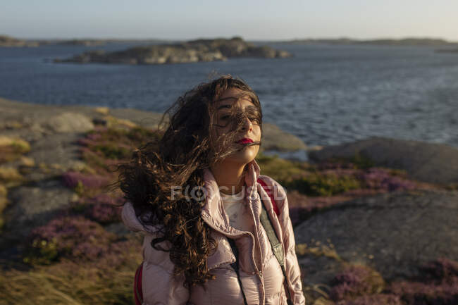 Seitenansicht einer Frau in lässiger Kleidung, die am Seeufer steht und an sonnigen Tagen die Brise genießt und in die Kamera blickt — Stockfoto