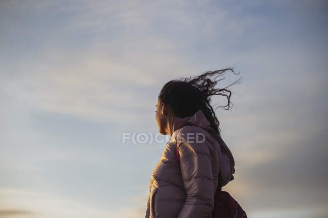 From below side view of female wearing casual clothes standing enjoying breeze on sunny day and looking away — Stock Photo