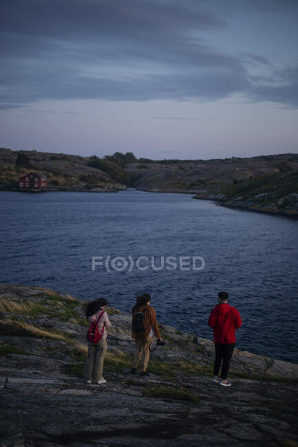 Back view of anonymous traveler couple in casual outfit with photo cameras in hands walking down rocky coast to sea and admiring amazing view — Stock Photo