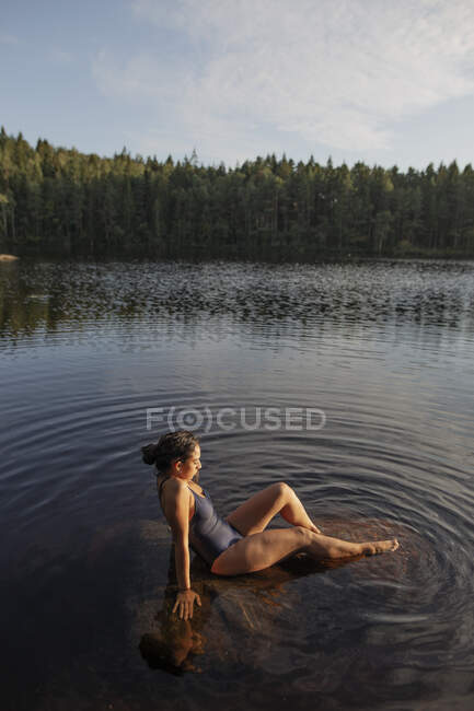 Сверху вид на стройную женщину в купальнике, сидящую с закрытыми глазами в спокойной воде озера, наслаждаясь закатом и величественными пейзажами — стоковое фото