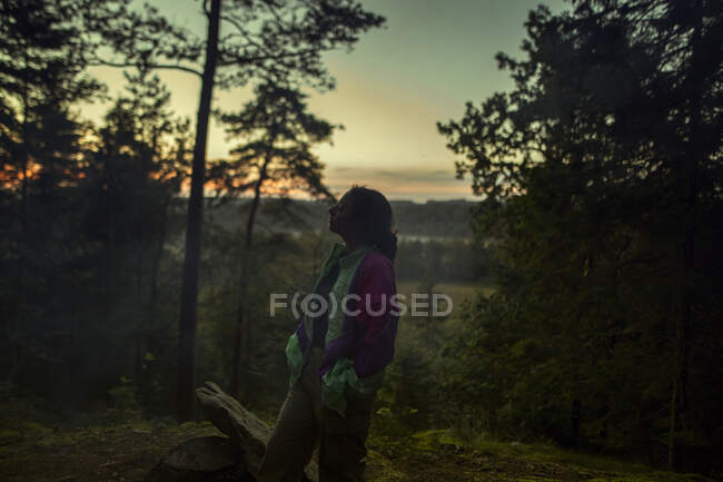 Seitenansicht einer ruhigen Reisenden in Freizeitkleidung, die während der Sommerferien mit geschlossenen Augen auf einem Hügel im Wald steht — Stockfoto