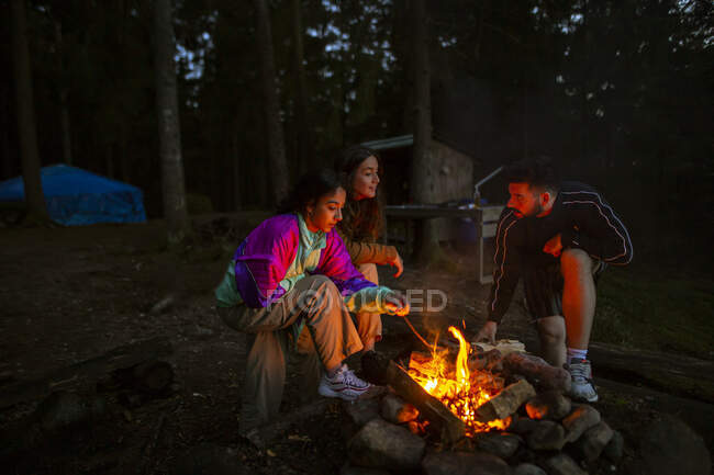 Gesellschaft von freundlichen Menschen in lässiger Kleidung, die sich am Lagerfeuer im Holz versammeln, während sie Feuer machen und sich am Abend aufwärmen — Stockfoto