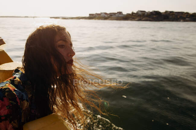 Вид сбоку женщины в повседневной одежде, стоящей на набережной и наслаждающейся бризом в солнечный день и отводящей взгляд — стоковое фото