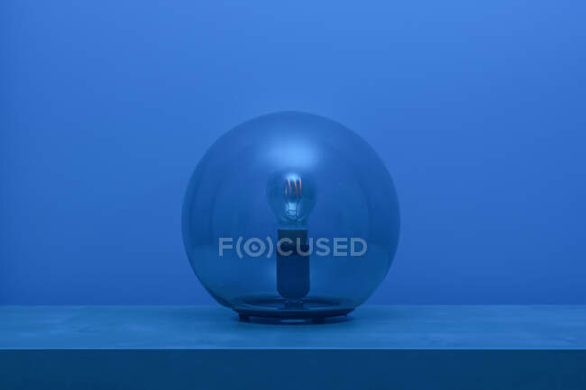 Сучасний вимкнений люстр з лампочкою всередині тонкої прозорої скляної сфери посередині полиці в синій кімнаті на сутінках. — стокове фото