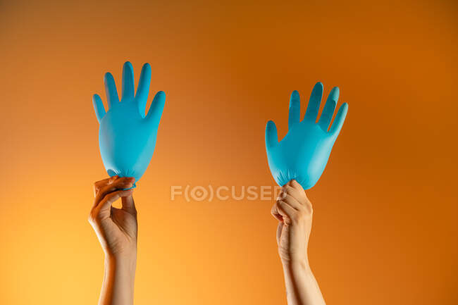 Pessoa sem rosto com balões feitos de luvas médicas mostrando gesto de mão acenando no fundo laranja — Fotografia de Stock