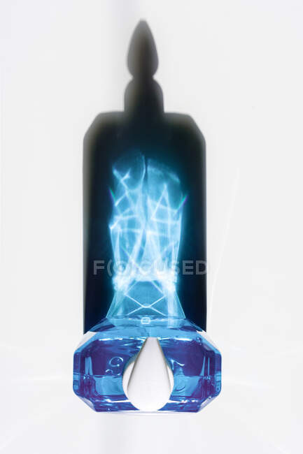Draufsicht auf transparente Flasche mit blauer Seifenflüssigkeit, die leuchtende Kristallschatten auf weißer Oberfläche reflektiert — Stockfoto