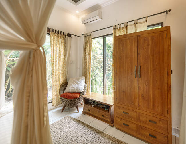 Інтер'єр спальні з дерев'яним шафою і зручним плетеним кріслом з подушками — стокове фото