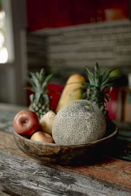Tigela de madeira com melão fresco, maçãs e abacaxi colocado na mesa de terraço de verão em Bali — Fotografia de Stock