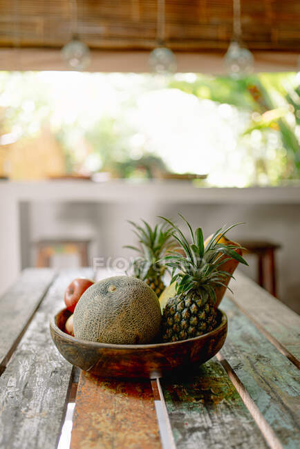 Cuenco de madera con melón fresco y piñas colocado en la mesa de terraza de verano en Bali - foto de stock