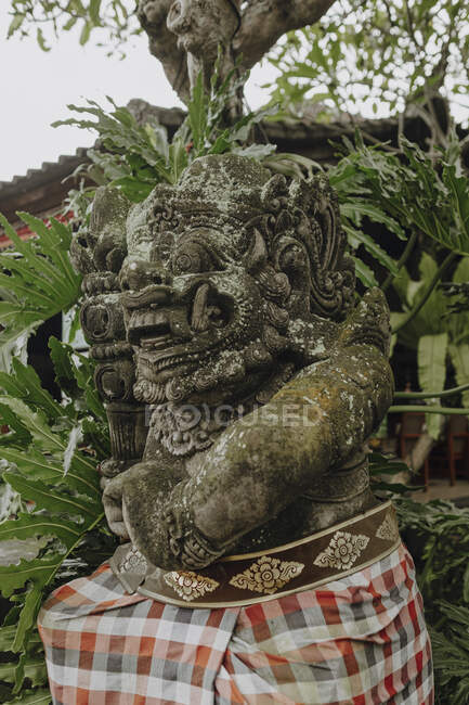 Baixo ângulo de estátua de Demônio cercado por folhagem tropical verde em Bali — Fotografia de Stock