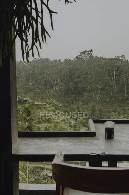 Сверху терраса с деревянными стульями и столами возле бунгало с соломенной крышей в окружении тропических растений в мрачный день на Бали — стоковое фото
