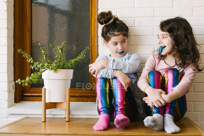 Two smiling sisters sticking out a blue tongue after eating a blue bubble gum — Stock Photo