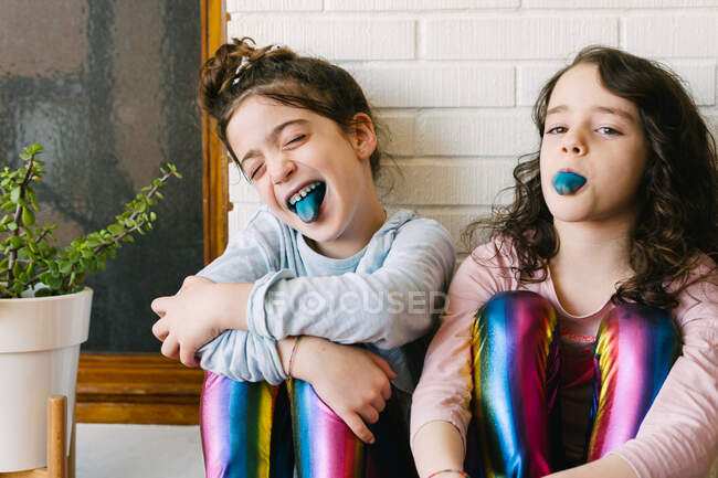 Duas irmãs sorridentes saindo de uma língua azul depois de comer uma pastilha elástica azul — Fotografia de Stock