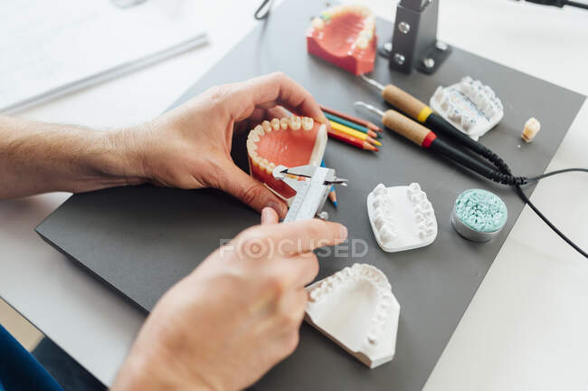 З понад врожаю студент стоматології за допомогою калібрування для вимірювання зубного протезу під час роботи за столом з інструментами під час уроку. — стокове фото
