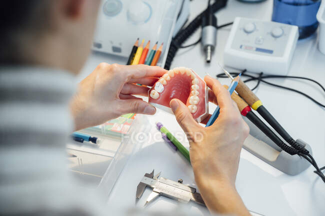 Crop unrecognizable student holding denture and a pencil while sitting at table during dentistry class — Stock Photo