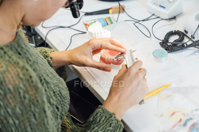 From above of crop male dentistry student using caliper for measuring dental prosthesis while working at table with tools during class — Stock Photo