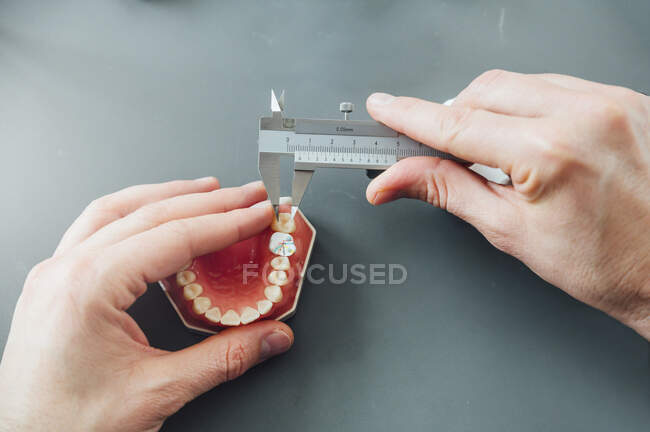From above of crop male dentistry student using caliper for measuring dental prosthesis while working at table with tools during class — Stock Photo