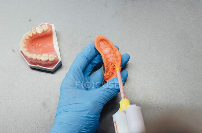 Vista de arriba hacia atrás del ortodoncista masculino de cultivo usando equipo profesional mientras trabaja con yeso dental en laboratorio moderno - foto de stock