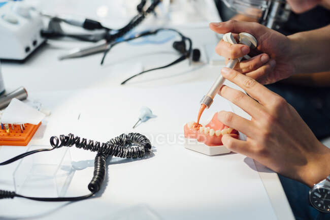 Vista de arriba hacia atrás del ortodoncista masculino de cultivo usando equipo profesional mientras trabaja con yeso dental en laboratorio moderno - foto de stock