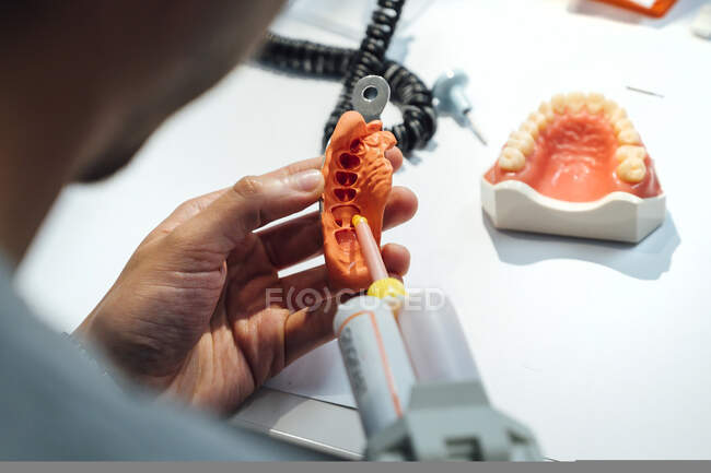 С обратной стороны вид на растениеводство мужчины-ортодонта с использованием профессионального оборудования при работе с зубным литьем в современной лаборатории — стоковое фото