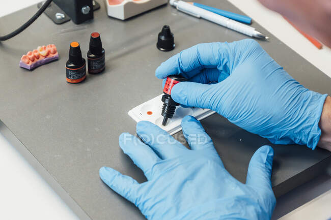 Von oben der Pflanzenzahnmediziner in Schutzhandschuhen mit buntem Zahnleim oder Gel beim Üben im modernen Labor — Stockfoto