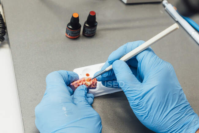 Do acima mencionado ortodontista irreconhecível pintando dentes artificiais sobre a mesa no laboratório moderno — Fotografia de Stock