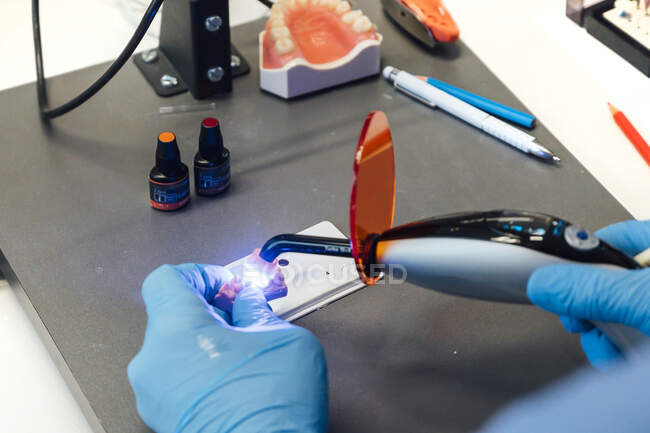З верху стоматологічного стоматолога в захисних рукавицях, використовуючи ультрафіолетовий інструмент, під час роботи з зубними імплантатами під час занять у лабораторії. — стокове фото