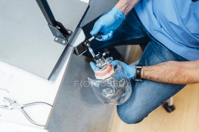 From above of crop male dentistry student in uniform and gloves preparing dental simulator for treatment during work in modern classroom — Stock Photo