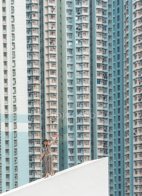 Mujer ondeando en vestido de rayas blancas y oscuras en el techo inclinado de hormigón y mirando a la cámara en Hong Kong en China - foto de stock